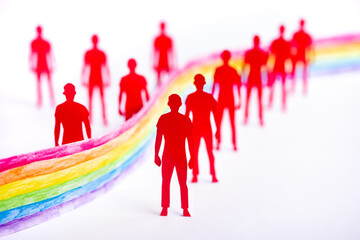 Paper cut-out figures standing around the hand painted lgbt colored ribbon.