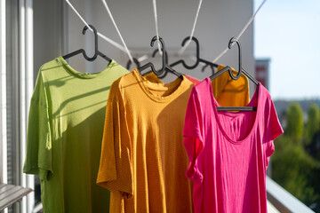 Three colorful t-shirts hanging to dry outside on the balcony. Drying clothes on the terrace in the city. - 648592143