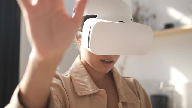 Beautiful young girl wearing virtual reality headset. Augmented Reality. Happy cute female touch something using modern 3D vr glasses indoors. Woman playing using VR goggles at home office. Sunny day