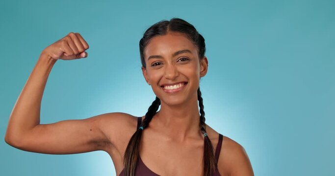 Arm, smile and kiss with a woman personal trainer in studio on a blue background for fitness success. Portrait, smile and exercise with a happy young sports person flexing her bicep for motivation