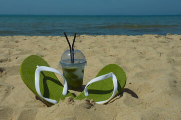 a glass of lemonade with a straw and summer flip-flops on the seashore, sunny beach, summer...