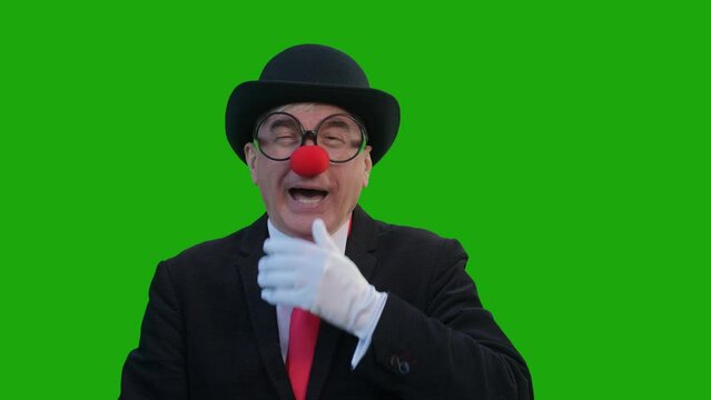 An elderly man in a clown costume laughs against a green background. Chromakey. 