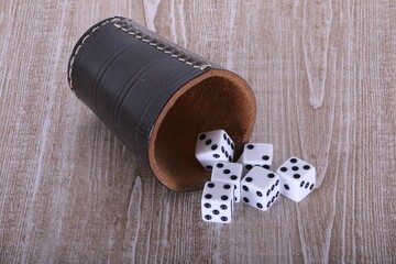 Leather dice cup lies on the wooden table and six white dice fall out
