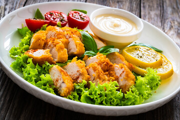 Seared breaded chicken nuggets with mayonnaise and fresh vegetables on wooden table
