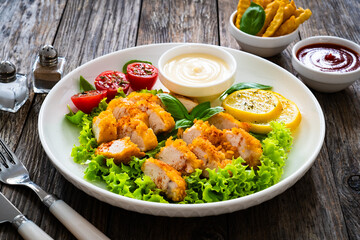Seared breaded chicken nuggets with mayonnaise and fresh vegetables on wooden table

