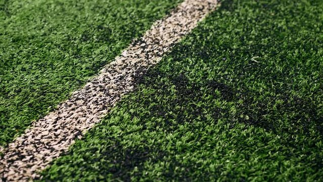 close-up of a hand running across a football synthetic grass with a rubberized texture