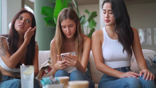 Three women engrossed in their phones while sitting on a couch