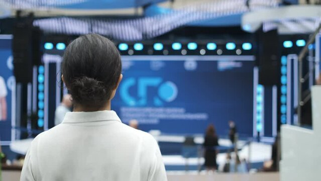 Female speaker goes on stage. Forum on business development. Hall is full. View from the back of auditorium with people at a conference or presentation. International economic business forum. Indoors