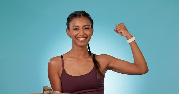 Arm, documents for membership and a woman personal trainer in studio on a blue background for sign up. Portrait, smile and fitness with a happy young sports person flexing her bicep for motivation
