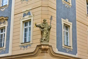 Religious Catholic sculpture of a monk on the corner of a historic building with blue and beige walls, and with decorative elements on the windows. Prague, Czech Republic, October 2022