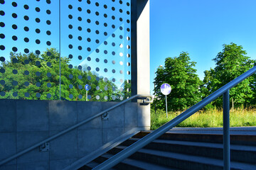 Modern technological structure made of concrete walls, stairs and glass against a background of blue sky and trees. Exit from the underpass. Poland, Poznan, June 2022.