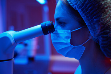 Woman in a medical uniform looks through powerful microscope eyepiece