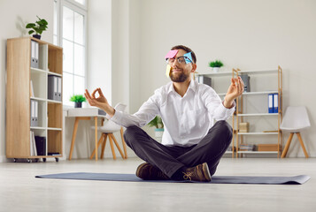 Funny busy man with sticky reminder notes on face sitting on yoga mat floor in his business office,...