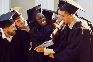 Group of happy and joyful university friends hugging after graduation ceremony. Multiracial young...