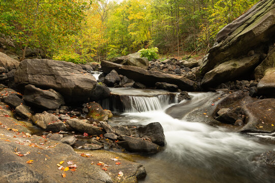 A small peaceful waterfall surrounded by tall trees just beginning to turn autumn colors falling over tumbled boulders in Nay Aug park in Scranton PA. USA.