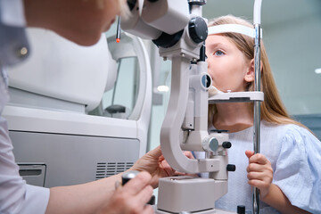 Licensed ophthalmologist conducting ocular examination of little girl