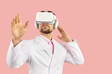 Virtual reality technology. Serious young elegant man touches air during virtual reality isolated on pink background. Male VR user in white formal suit uses modern device in his work. Banner.