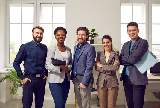 Portrait of happy confident and successful multiracial business team posing in office. Smiling men and women in smart casual clothes and with clipboard stand in row in business center.
