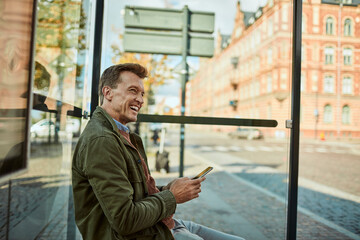 Middle aged businessman using the smartphone while waiting for his bus at the bus stop
