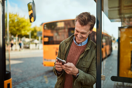 Middle aged businessman using the smartphone while waiting for his bus at the bus stop