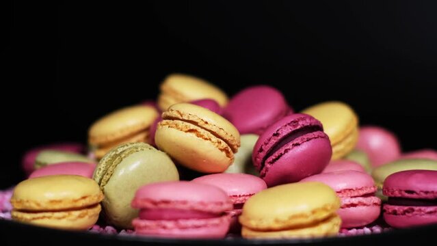 Close-up of rotating fresh macaron cookies. Traditional french desserts from almond dough. Slow motion of colourful sweet macaron cakes spinning with black copy space. French cuisine or sweets concept