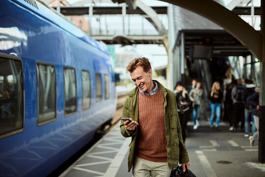 Middle aged businessman using a smartphone while waiting for his train at the train station