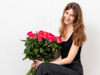 Young attractive girl with a bouquet of red roses on a white background. A happy girl with a bouquet of roses is smiling. The concept of happiness, joy and celebration