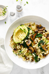 Couscous with avocado, spinach and sauteed champignon mushrooms with onion, top down view