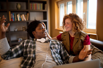 Young interracial couple using the laptop on the couch in the living room at home