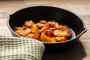 Fried pineapple in a cast iron frying pan. On a wooden chopping board in a kitchen