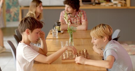 Obraz na płótnie Canvas Two children playing chess in cafe. Chess is a strategic game that stimulates critical thinking, problem-solving, and cognitive skills. Kids mentally stimulating indoor activity. People lifestyle.