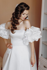 Beautiful model girl with long curly hair in a fashionable wedding dress. Vertical close-up portrait