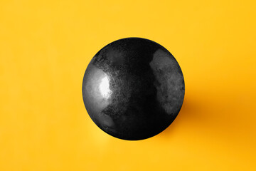 Black metallic sphere on yellow background