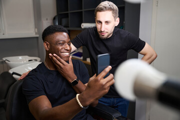 Fototapeta premium Satisfied African American guy takes a selfie in a barbershop