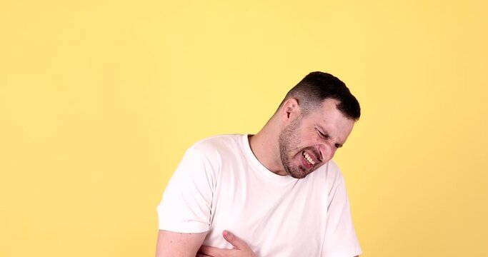 Bearded guy feeling sudden stomach pain, severe abdominal distress, suffering constipation, gastritis, pancreatic diseases. Studio shot isolated on yellow background.