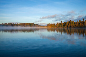 Trees and shoreline in early morning fog and light on a beautiful blue northern Minnesota lake in September