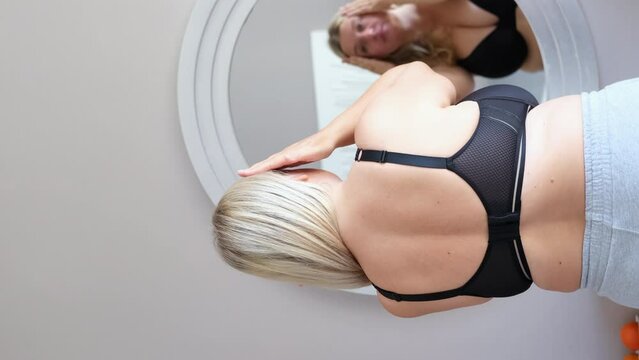 Young blond overweight woman in underwear examines her abs in front of the mirror 