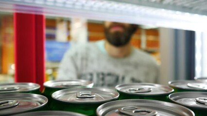 Close-up of many cans of energy drink or beer in the store fridge and a male buyer takes one