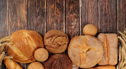 Poster Freshly baked whole grain homemade bread, assorted varieties of round sourdough bread with crispy crust and ears of rye and wheat on a wooden background with space for text, modern baking concept, © Светлана Балынь