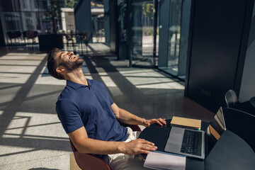 Cheerful handsome male sales manager working on laptop sitting in coworking during working day