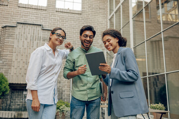 Cheerful coworkers discuss the project while use digital tablet standing on cafe terrace background