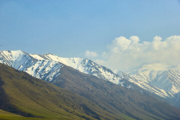 Fototapeta premium landscape against a mountain backdrop of high mountain ranges with snow-capped mountains and a blue sky with clouds