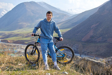 Fit and athletic teenager with a bicycle on the background of the highlands in the fresh air