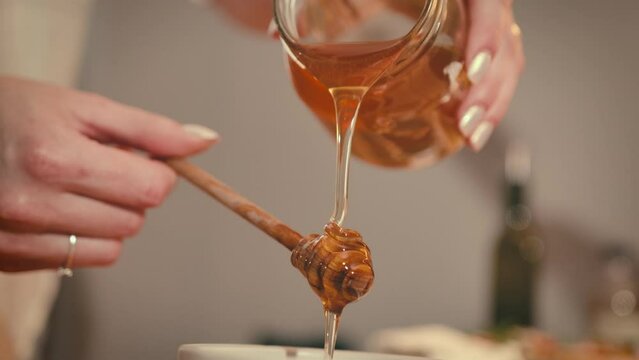Honey is dripping, pouring out of a glass jar. Close-up. Healthy organic thick honey dripping from a wooden honey spoon, close-up. Video shooting in 4K UHD. Slow motion. High quality 4k footage