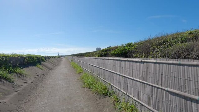 The image shows a straight bike path forward, surrounded by sand fences.