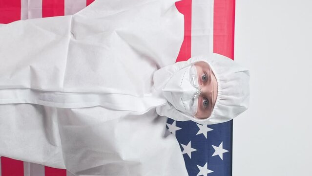 Vertical video. USA healthcare. United states medicine. Female virologist doctor woman in ppe suit with American flag isolated on grey background.