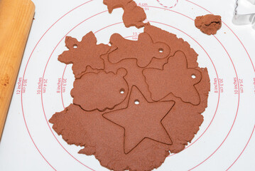 Cinnamon dough.  White pastry sheet with rolled cinnamon dough with ornament shape cut outs.  Star, Santa, Angel, snowflake, and gingerbread person. 