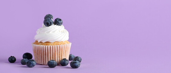 Tasty cupcake and blueberries on lilac background with space for text