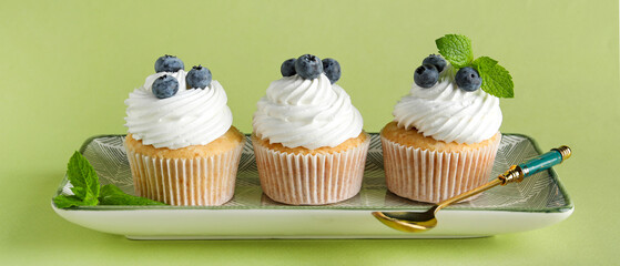 Tasty blueberry cupcakes on green background
