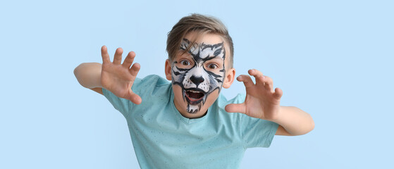 Funny little boy with face painting on light blue background © Pixel-Shot